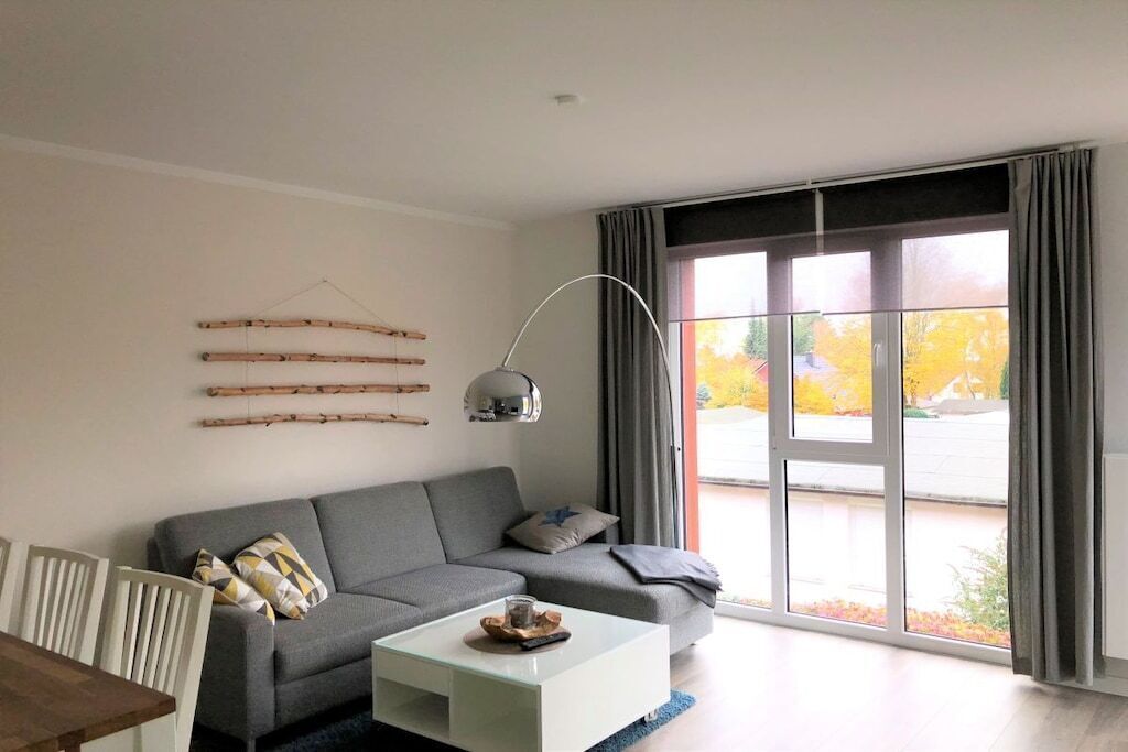 A modern living room with a grey sofa, a glass coffee table, and a large window with curtains.