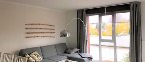 A modern living room with a grey sofa, a glass coffee table, and a large window with curtains.
