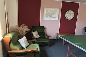 A room with a green chair, a small table, a ping pong table, and a wall clock. - Schulte Holiday Farm (Schmallenberg)
