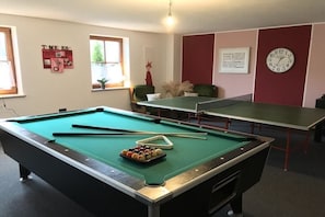 A pool table with billiard balls and cues, a ping pong table, and a wall clock. - Schulte Holiday Farm (Schmallenberg)