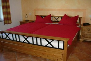 A bed with a wooden frame and red bedding, a nightstand with a lamp, and a wooden cabinet with drawers. - Schulte Holiday Farm (Schmallenberg)
