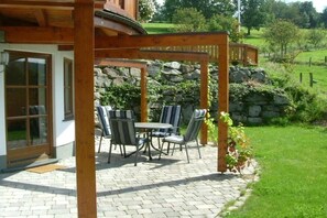 En uteplats med ett bord och stolar, en stenmur och en träpergola.