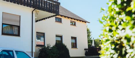 A white building with a tiled roof, a parked car, and a brick driveway.