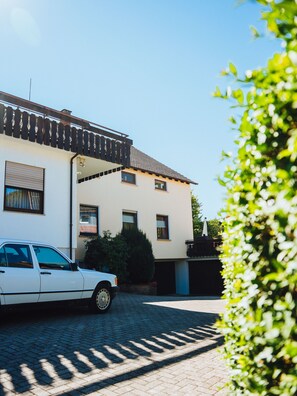 Een wit gebouw met een pannendak, een geparkeerde auto en een oprit van baksteen.