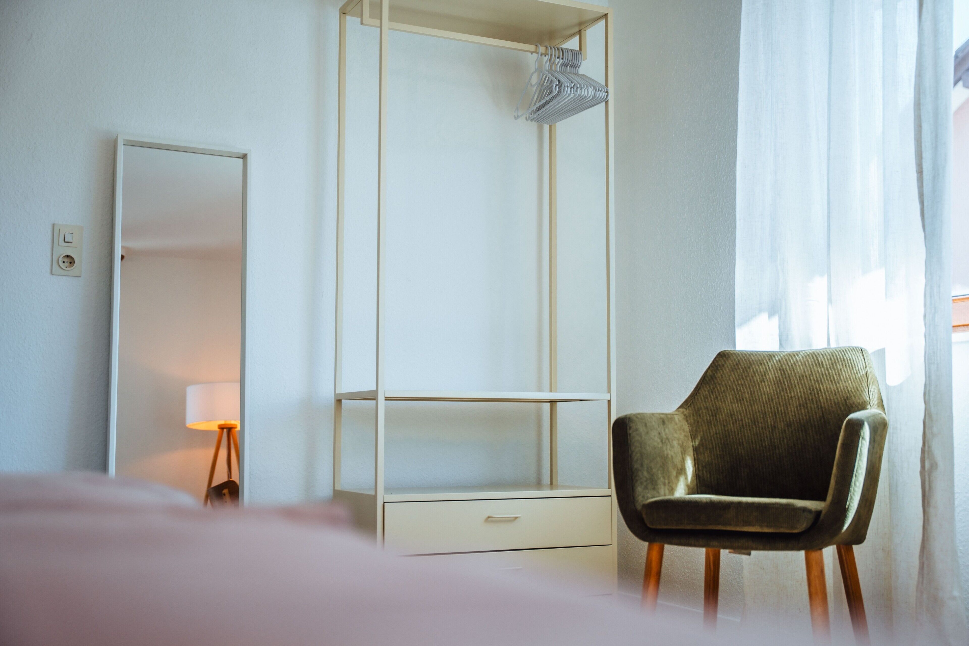 A hotel room with a bed, a chair, a wardrobe, a mirror, and a lamp.