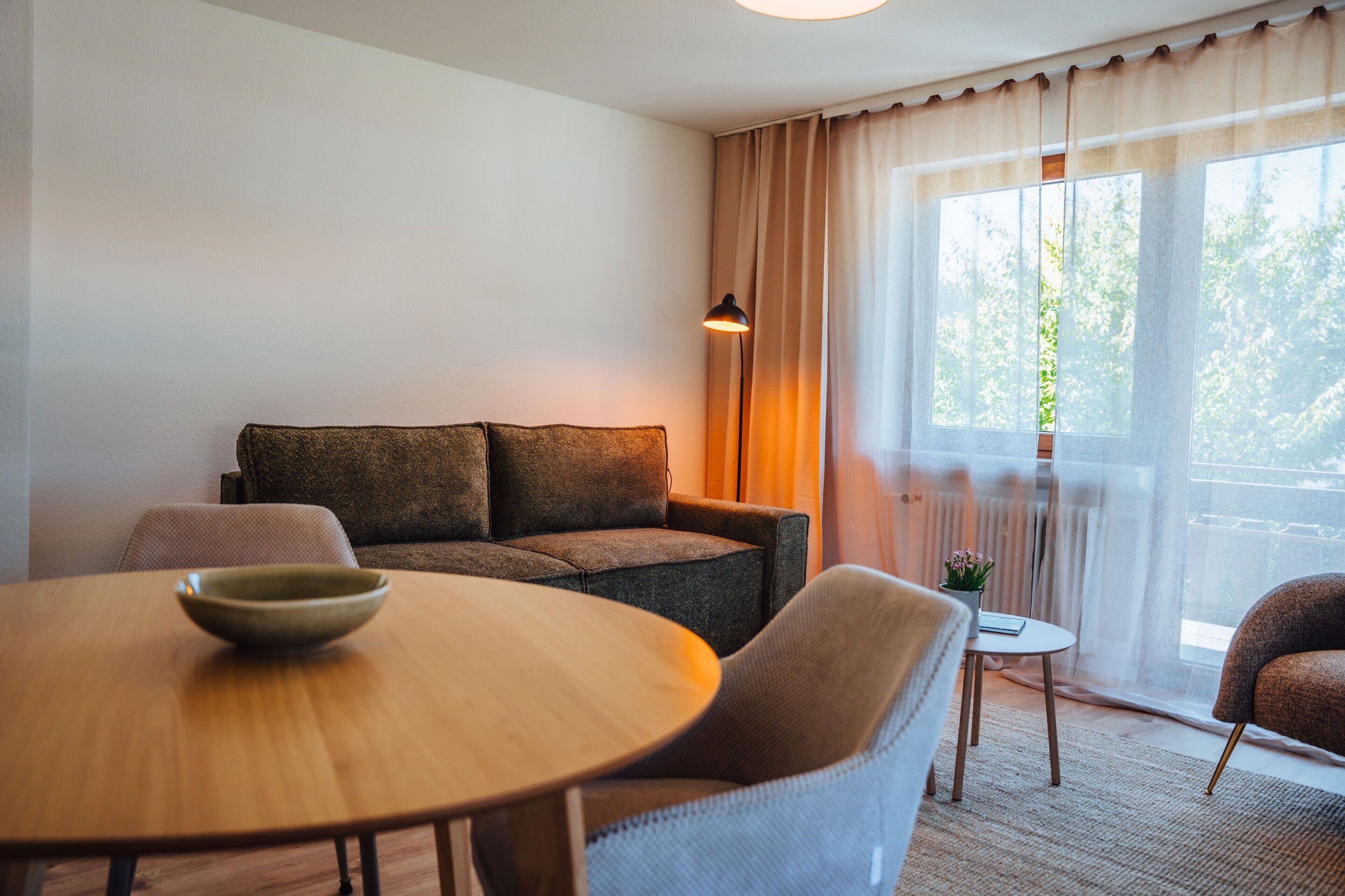 Un salon moderne avec un canapé, une table ronde et une petite table d’appoint agrémentée d’une plante.