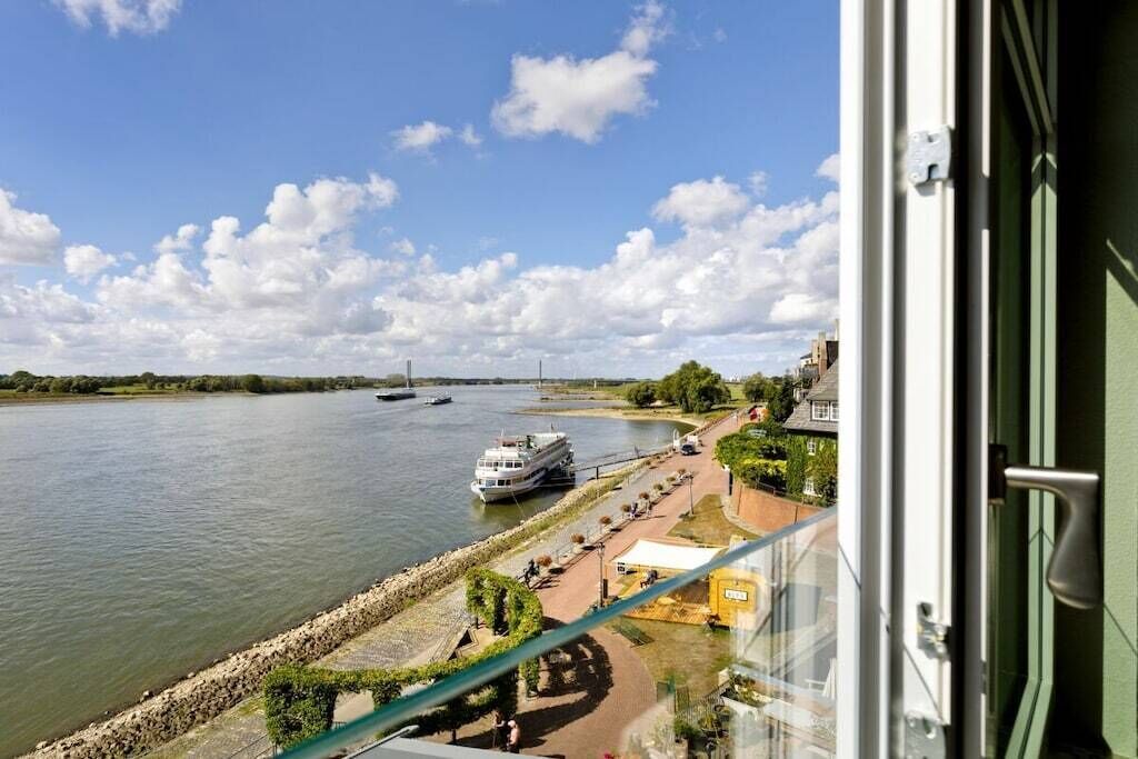 Un río con barcos, un paseo marítimo y edificios al fondo.