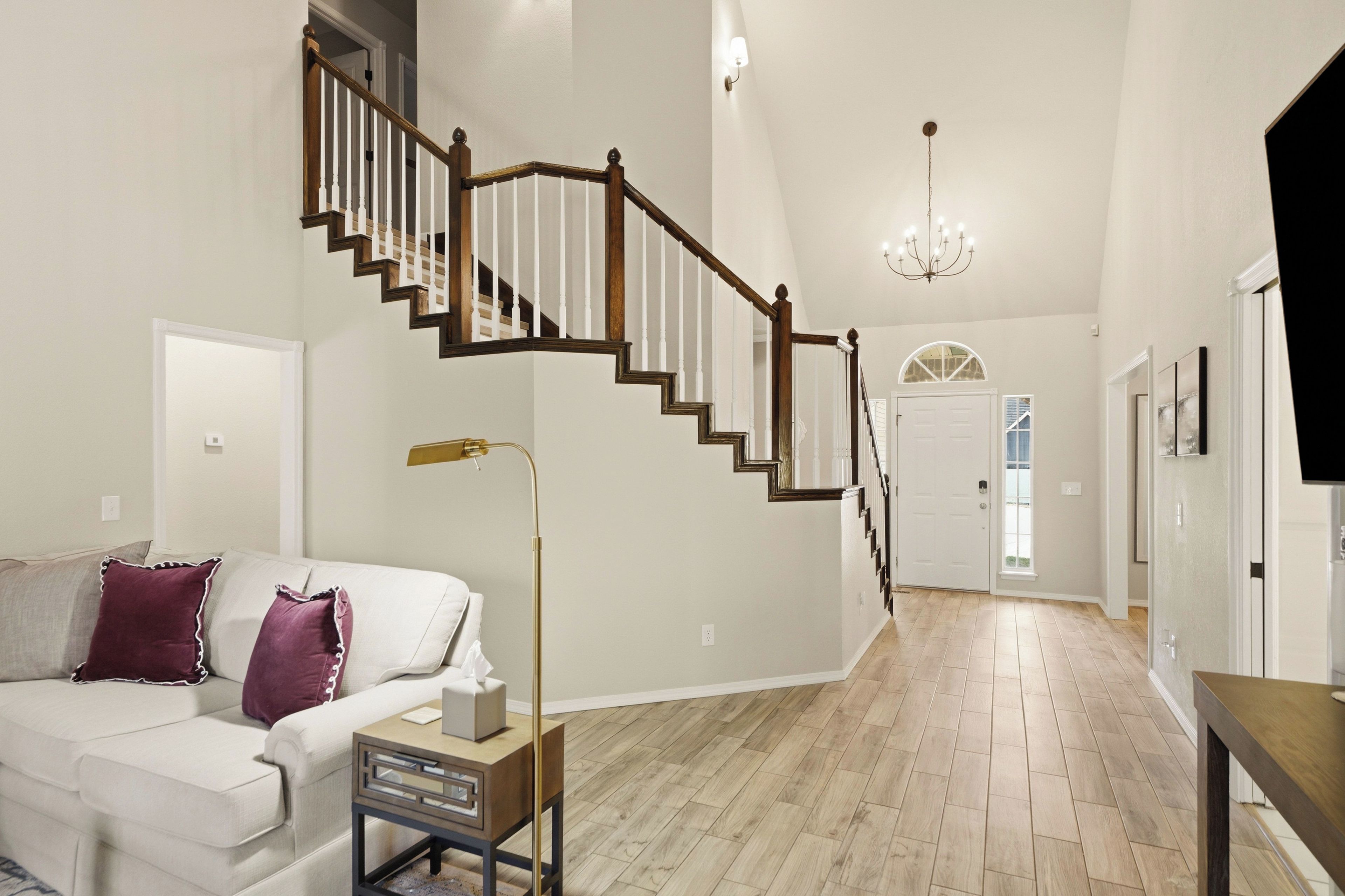Un salón amplio con una escalera de madera, un candelabro y un gran ventanal.