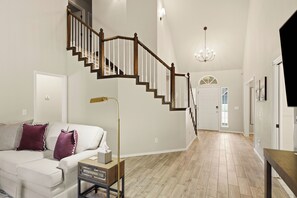 Ein geräumiges Wohnzimmer mit einer Holztreppe, einer Kandelaberleuchte und einem großen Fenster.