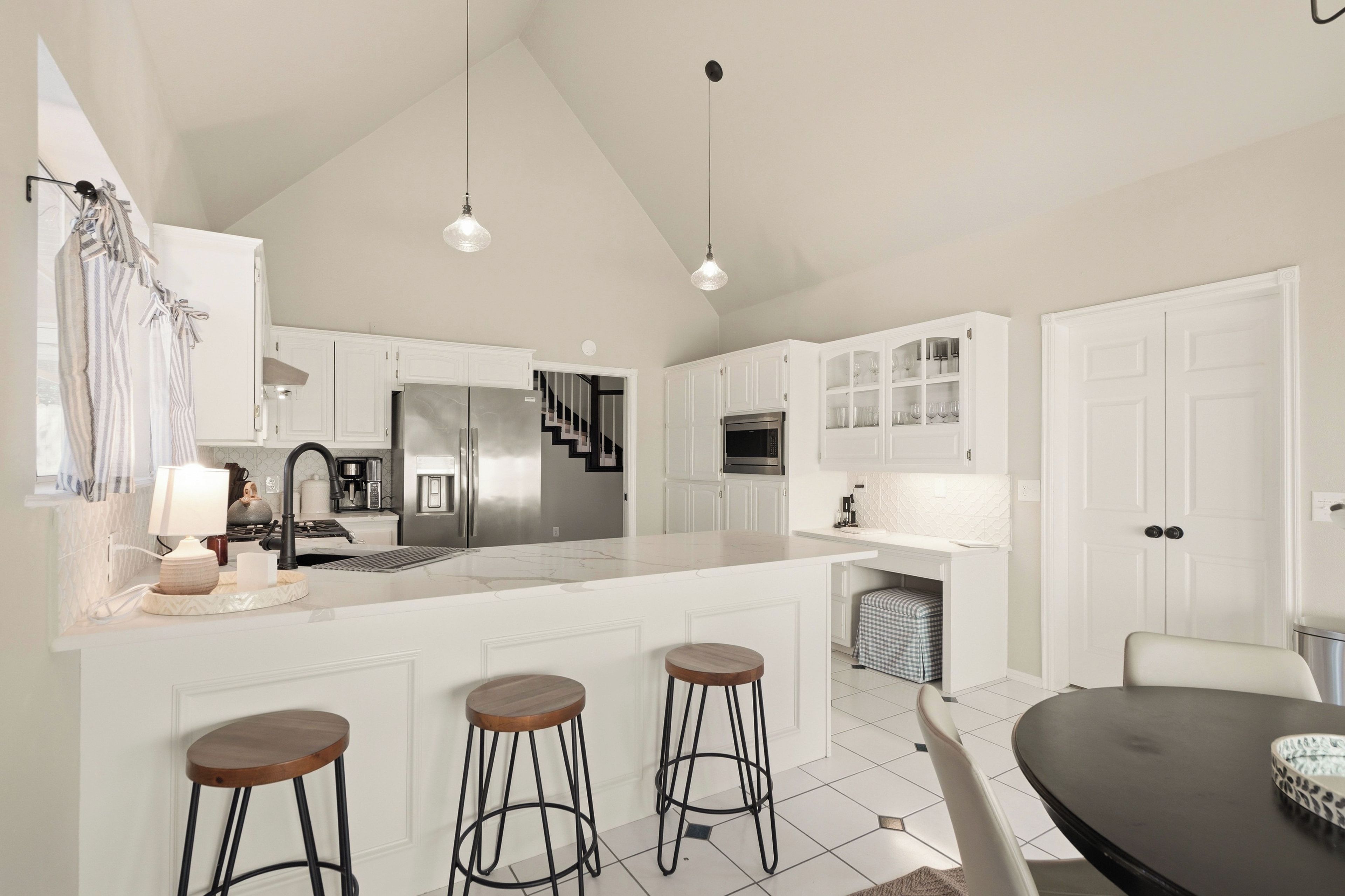 A modern kitchen with white cabinetry, stainless steel appliances, and a central island with stools.