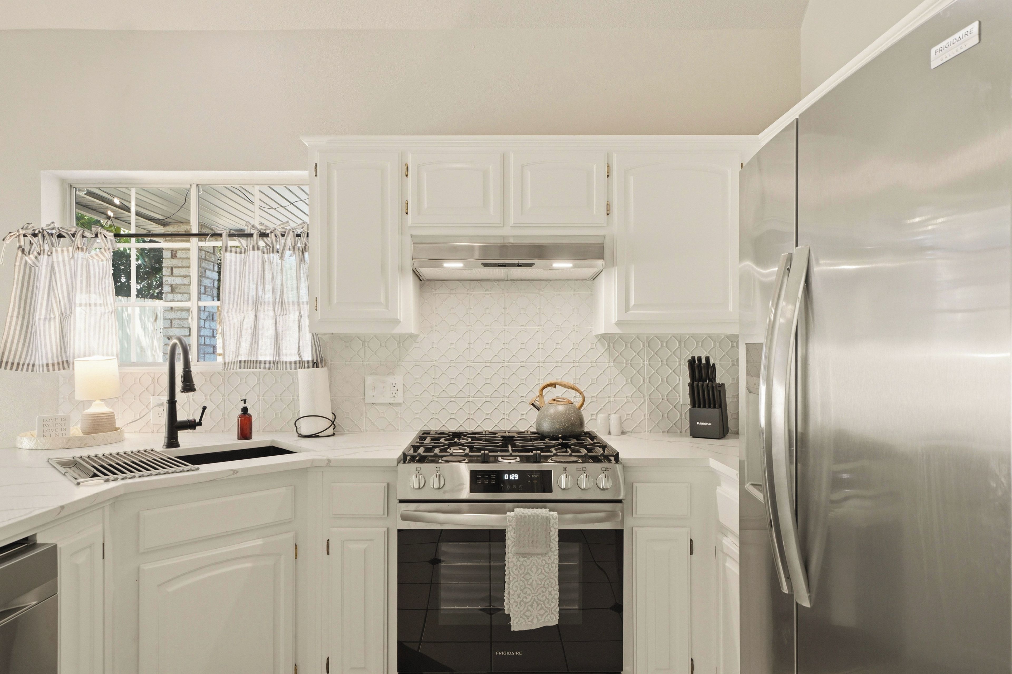 Una cocina con armarios blancos, un refrigerador de acero inoxidable, una estufa a gas y un horno empotrado.