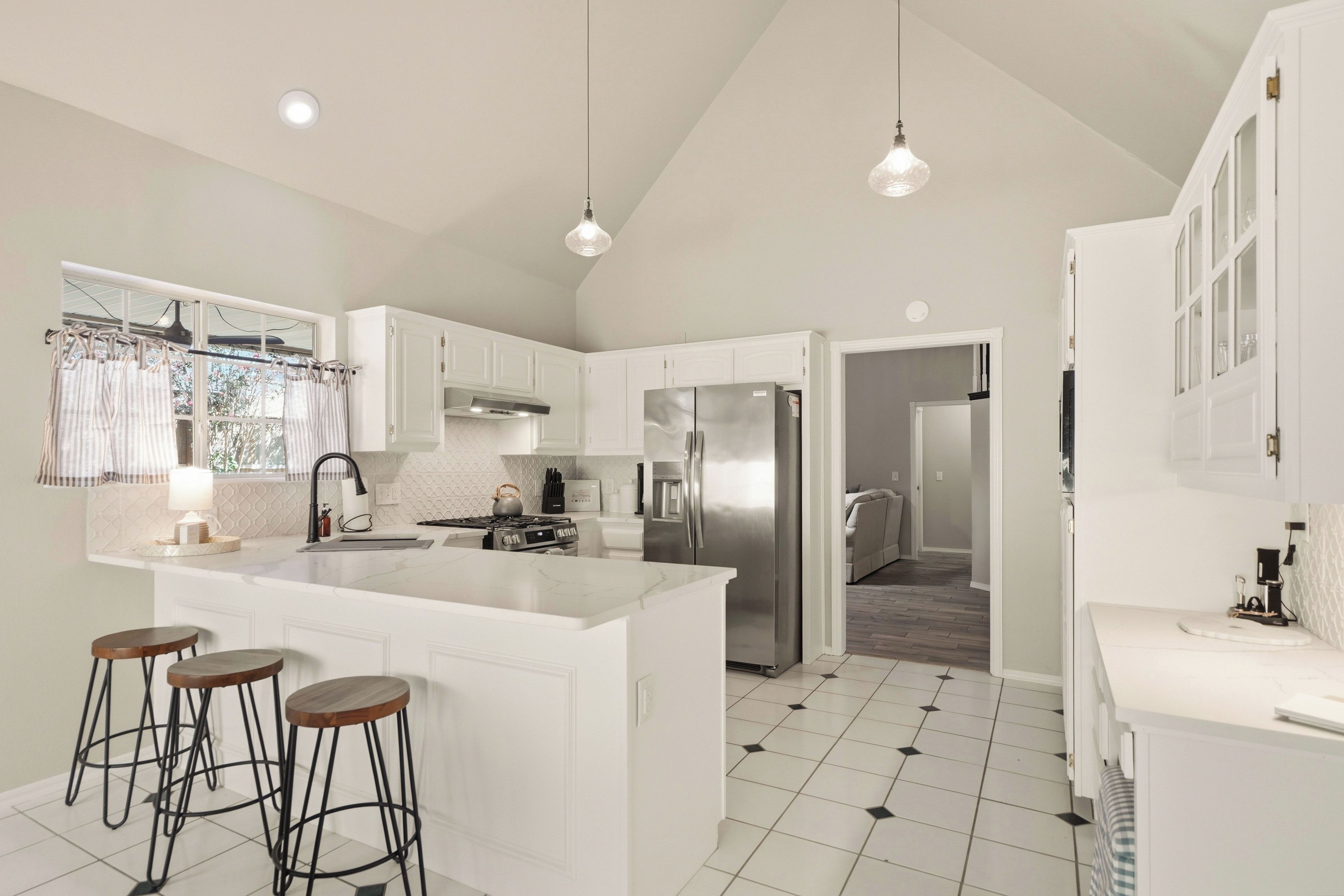 A modern kitchen with white cabinetry, a central island with stools, a stainless steel refrigerator, and pendant lighting.