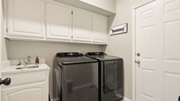 A laundry room with two black washing machines, a sink, and a cabinet above the machines.
