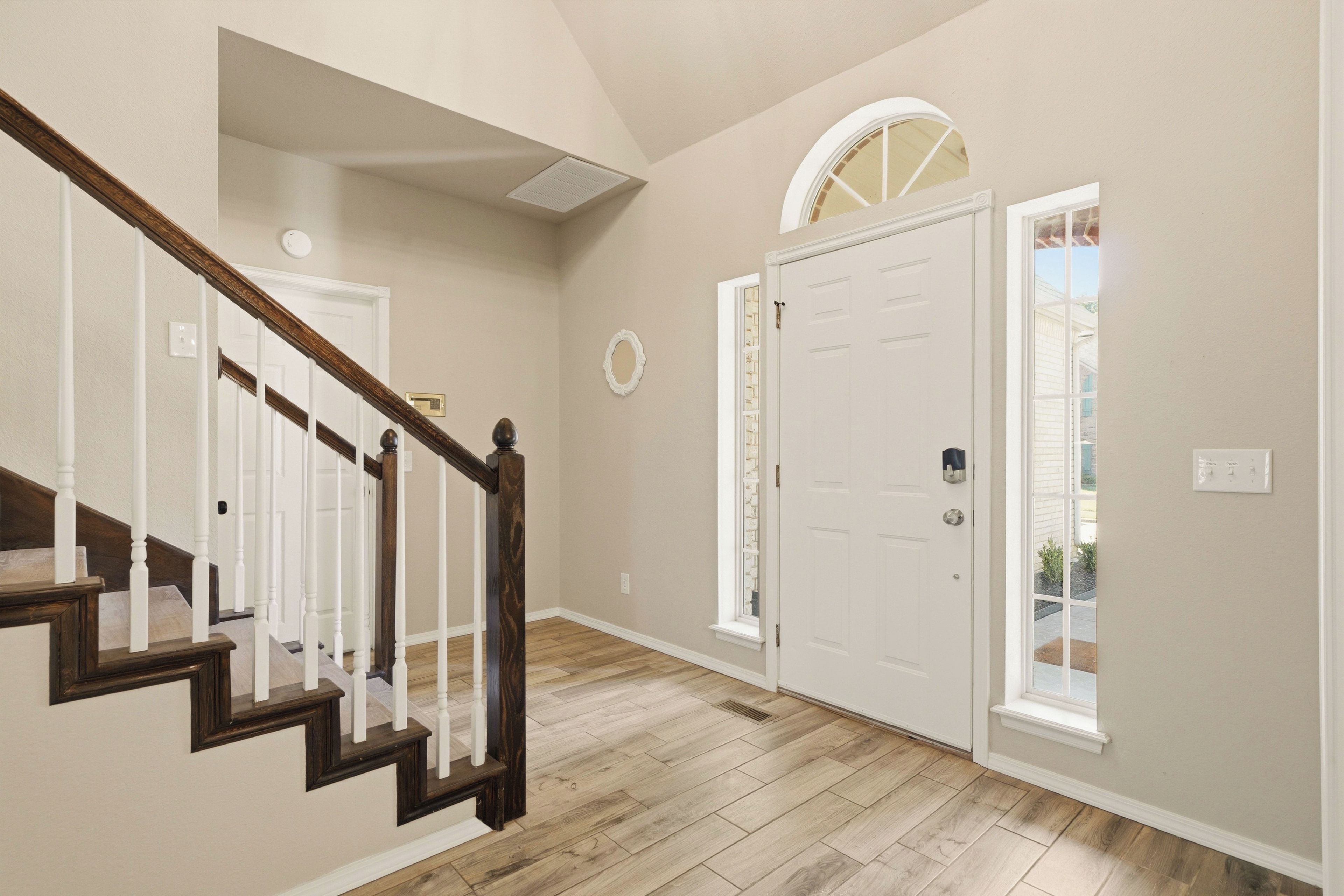 A hallway with a wooden staircase, a white door with a window, and a light-colored wall.