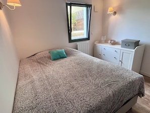 Een slaapkamer met een bed, een raam, een dressoir en wandlampen.