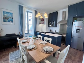 Een moderne keuken met een centraal eiland, witte stoelen en een eettafel voor vier personen.
