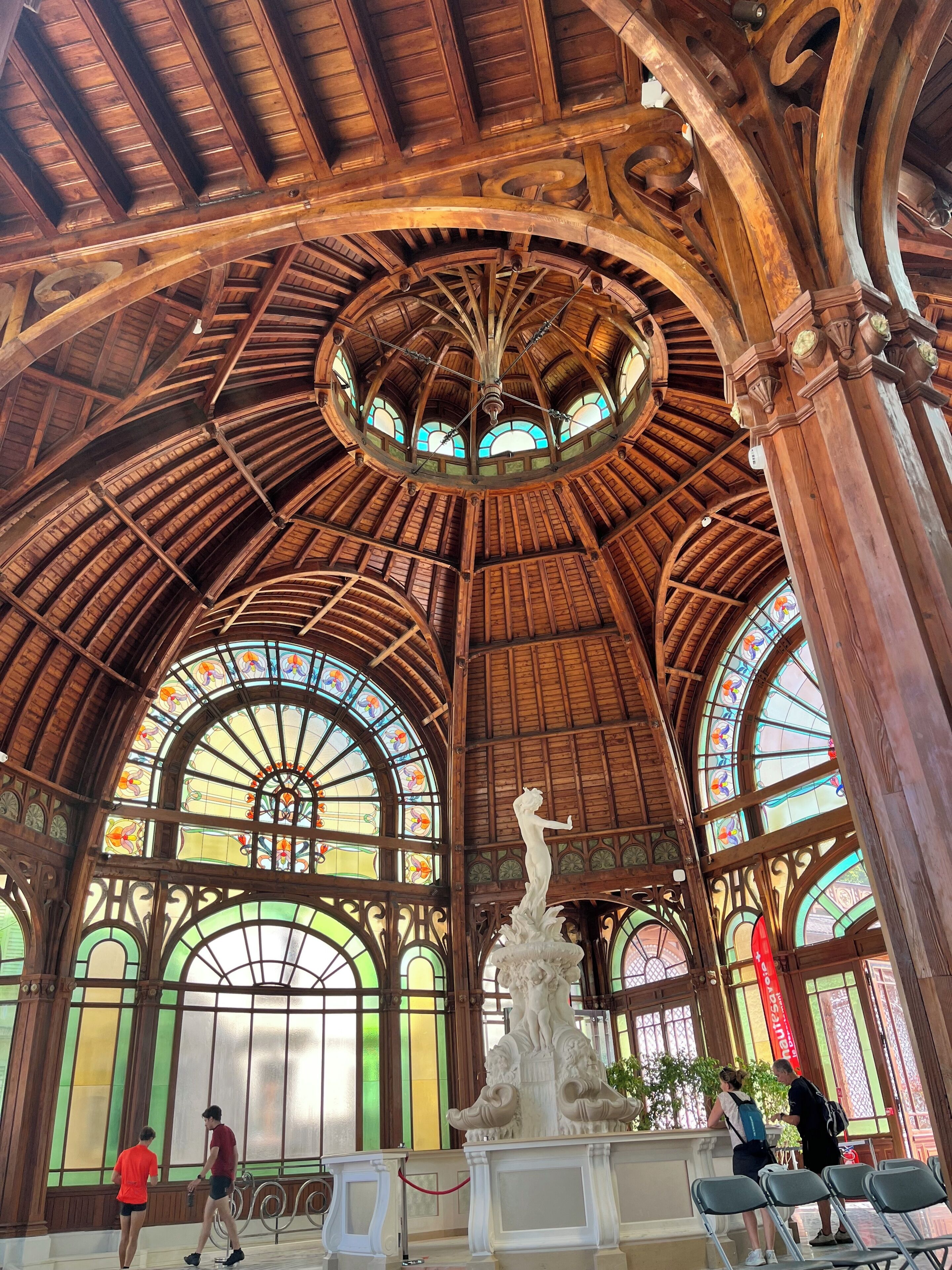 A grand hall with a high wooden ceiling, arched windows, and a central statue.