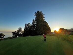 Een persoon op een golfbaan met uitzicht op een zonsondergang en bomen.