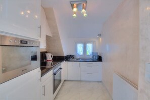 A compact kitchen with a built-in oven, a coffee maker, and a window with curtains. - Holiday apartment in Sylt with 1 bedroom (Wenningstedt)