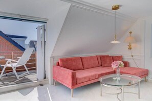 A modern living room with a pink sofa, a glass coffee table, and a view of a brick building outside. - Holiday apartment in Sylt with 1 bedroom (Wenningstedt)