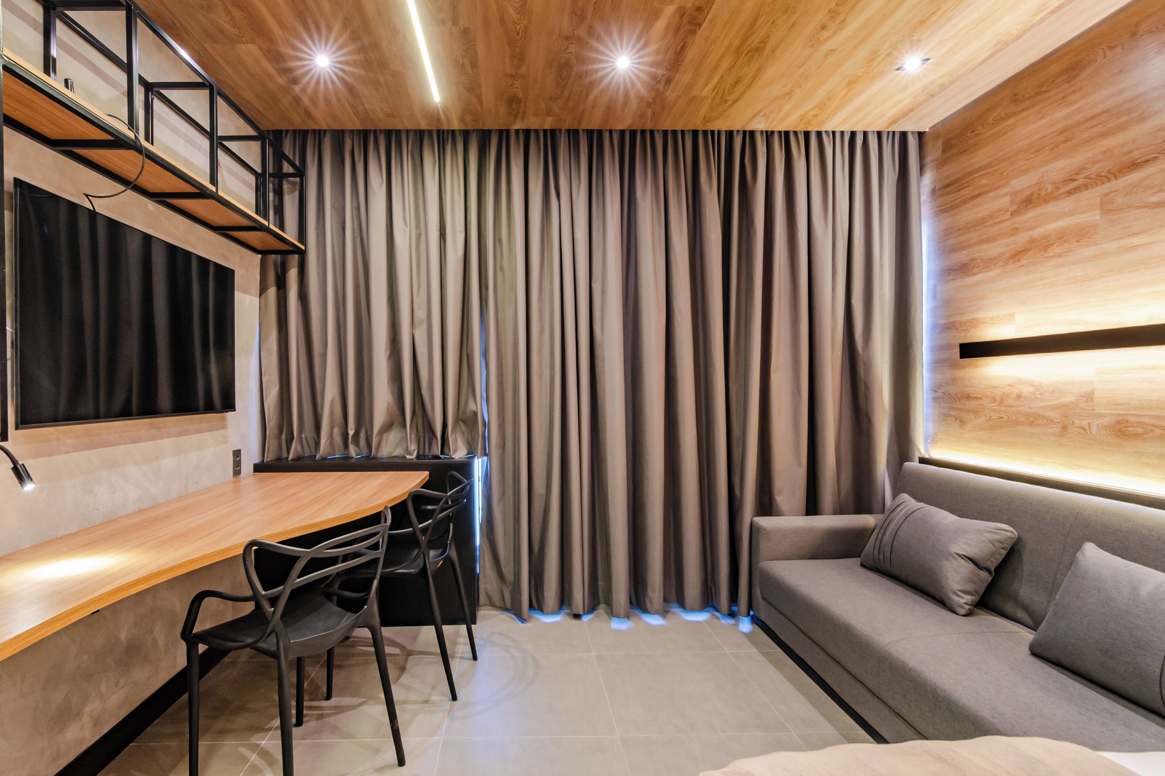 A modern interior with a wooden ceiling, a dining area with a table and chairs, a sofa, and a large window with curtains.
