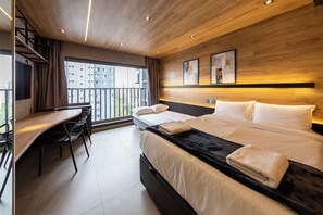 Una moderna camera d'hotel con un letto, una scrivania e vista sulla città.
