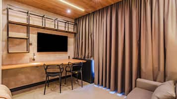 Ein moderner Wohnraum mit einem an der Wand befestigten Flachbildfernseher, einem Holztisch, zwei Stühlen, einem Sofa und einem großen Fenster mit Vorhängen.