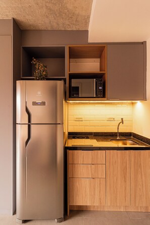 Una cucina compatta con frigorifero in acciaio inossidabile, forno a microonde e lavello con piano in legno.