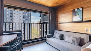 Una sala moderna con sofá, una mesa de comedor y sillas. Se aprecia una ventana grande con vistas a edificios altos.