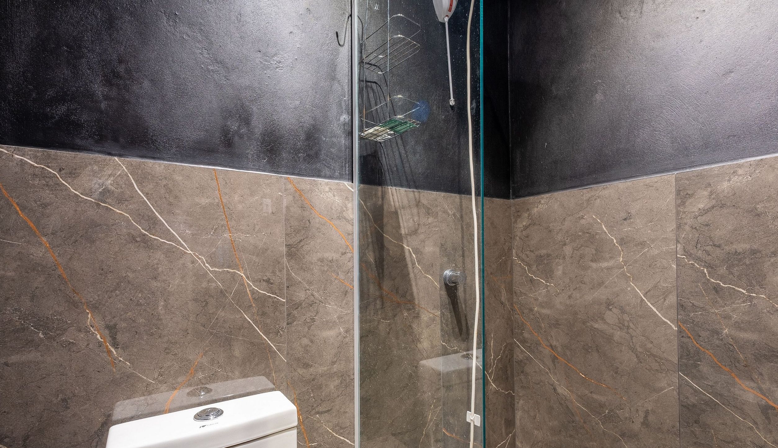 A bathroom with a glass shower enclosure, a white toilet, and marble-patterned walls.