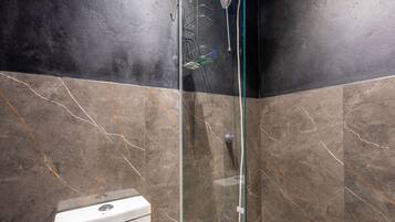 A bathroom with a glass shower enclosure, a white toilet, and marble-patterned walls.