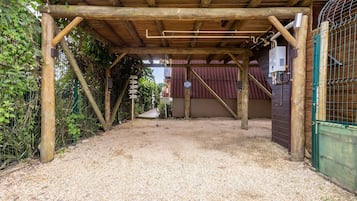 Een overdekt buitengebied met een grindvloer, houten balken en een metalen poort.
