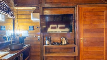 A wooden interior with a television mounted on the wall, a coffee maker, and a kettle on a shelf.