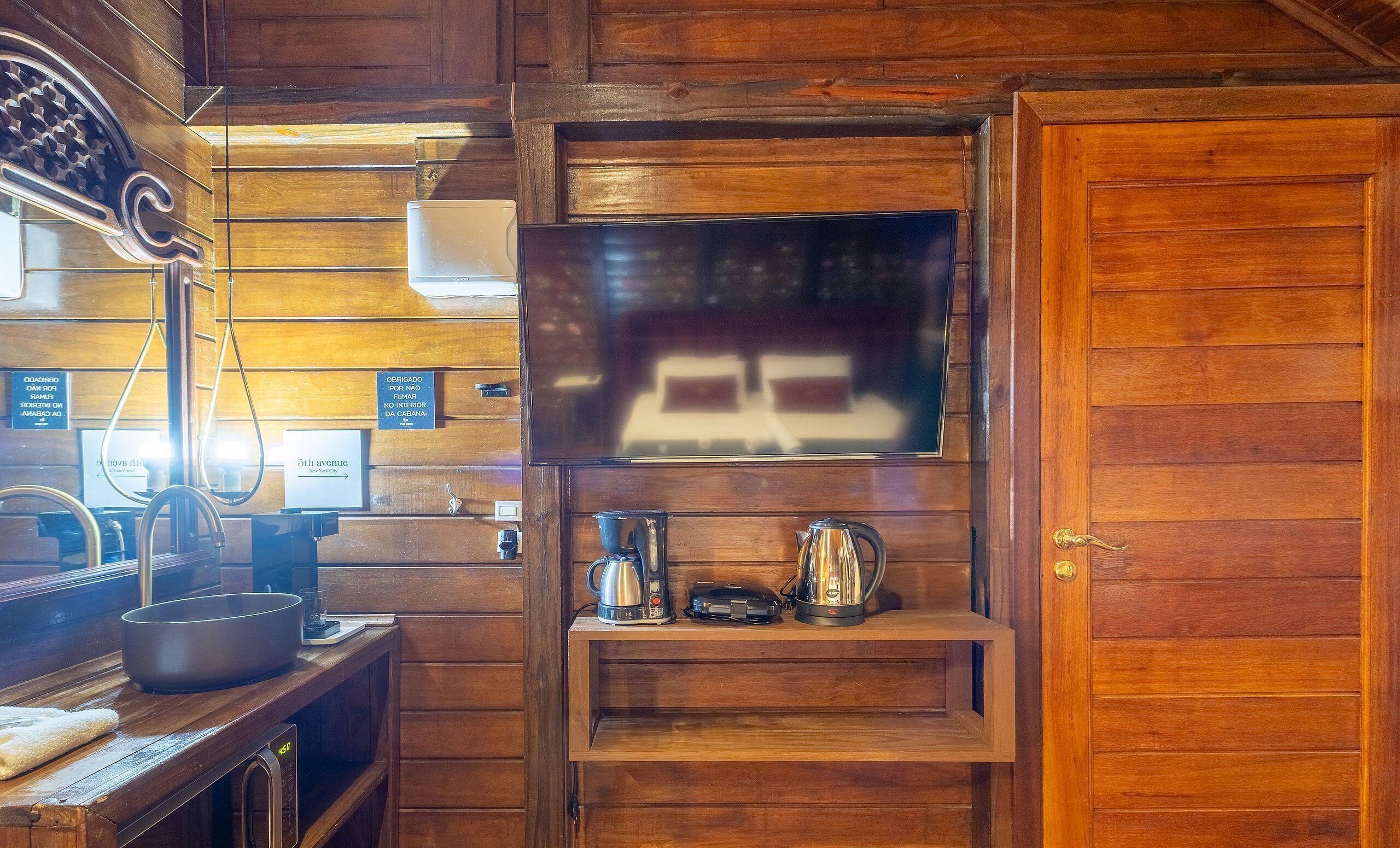 Interior em madeira com televisão na parede, cafeteira e chaleira em uma prateleira.