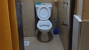 A small bathroom with a toilet, a shelf with cleaning supplies, and a blue cleaning tool. - Studio airbnb mirema drive (Nairobi)