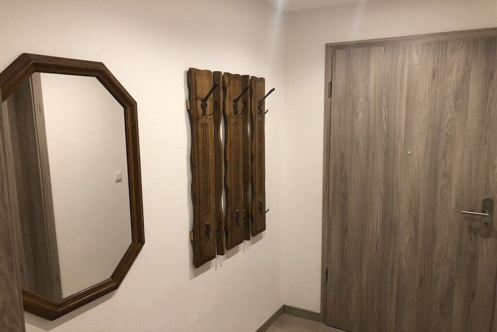 Une pièce dotée d’un grand miroir octogonal, d’une œuvre d’art murale en bois agrémentée de crochets, et d’une porte en bois.