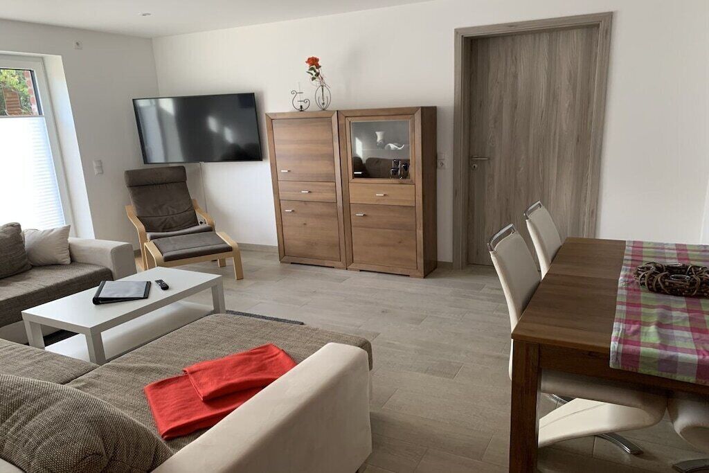 Un salon moderne comprenant un canapé, un fauteuil, un téléviseur, un meuble en bois et une table à manger avec des chaises.