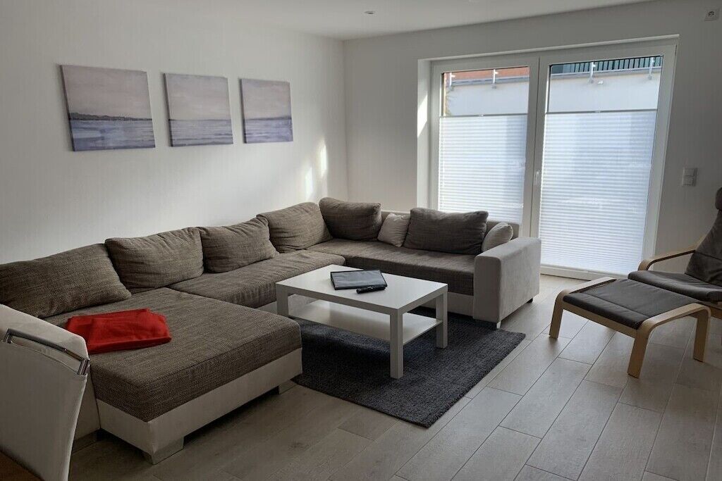 A modern living room with a sectional sofa, a small coffee table, and a chair. There are three paintings on the wall.