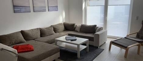 A modern living room with a sectional sofa, a small coffee table, and a chair. There are three paintings on the wall.