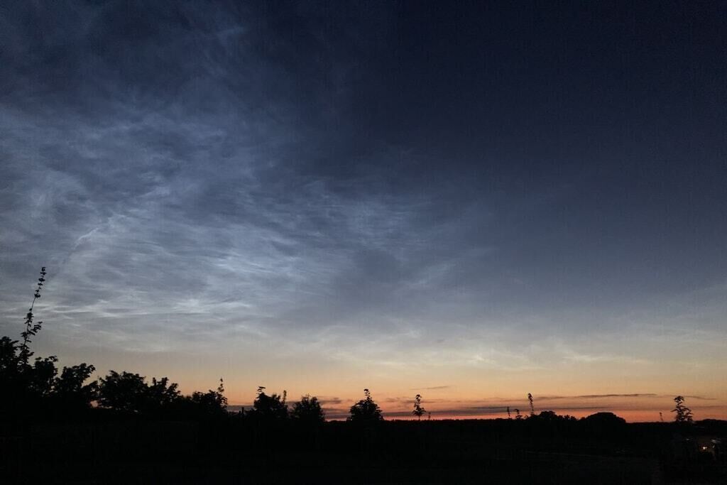 A twilight sky with clouds and silhouettes of trees.