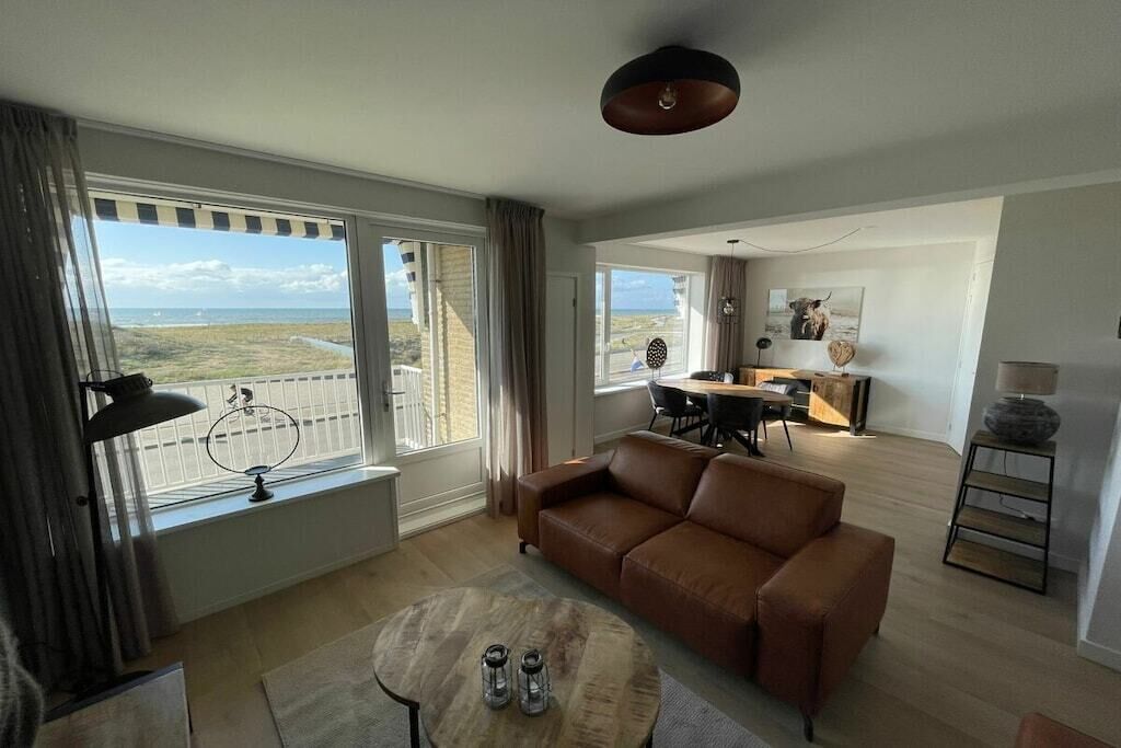 Ein Wohnzimmer mit braunem Ledersofa, einem runden Holztisch und einem Essbereich mit Tisch und Stühlen.