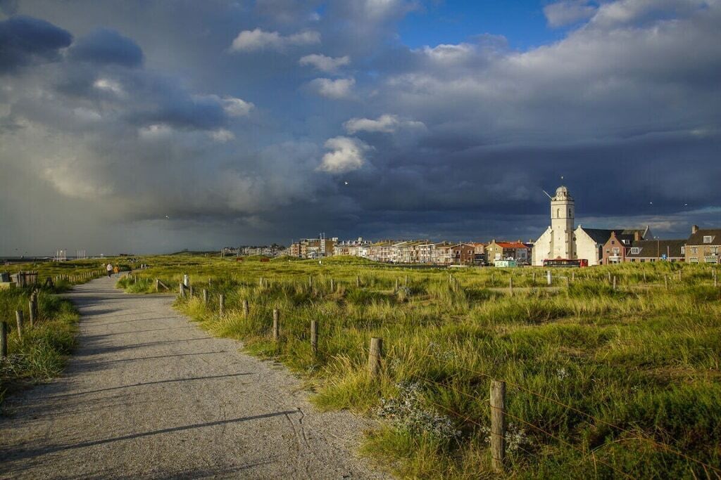 A coastal path leading to a town with a prominent white church and residential buildings.