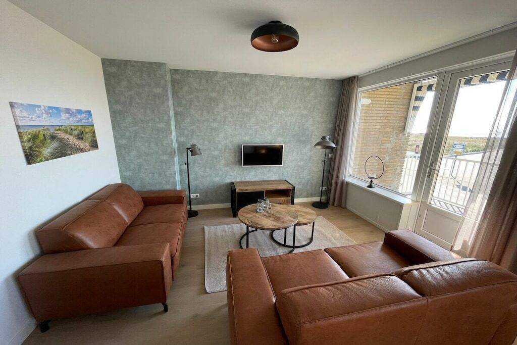 Ein modernes Wohnzimmer mit einem braunen Ledersofa, einem Holztisch, einem Flachbildfernseher und einem großen Fenster mit Blick.