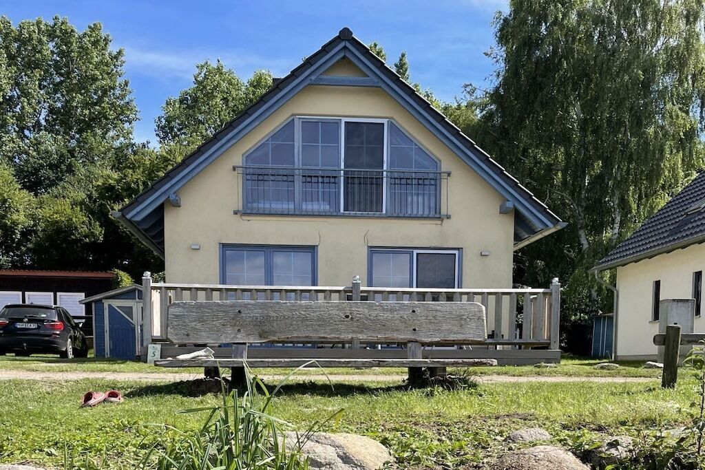 Une maison à deux étages avec un balcon, une clôture en bois et une voiture garée à l’arrière-plan.