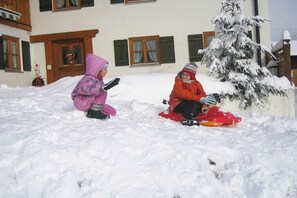 Two children sledding in a snowy outdoor area with a building in the background. - 4 - at the Füssen equestrian center (Weißensee-Füssen)
