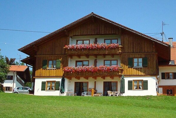 A two-story wooden building with balconies, a car parked in front, and a clear sky. - 4 - at the Füssen equestrian center (Weißensee-Füssen)