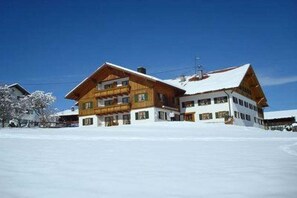 A multi-story wooden building with a snow-covered roof, surrounded by snow. - 4 - at the Füssen equestrian center (Weißensee-Füssen)