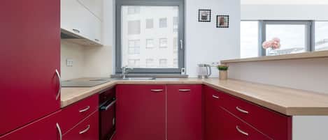 A compact kitchen with red cabinets, a wooden countertop, and a window with a city view.
