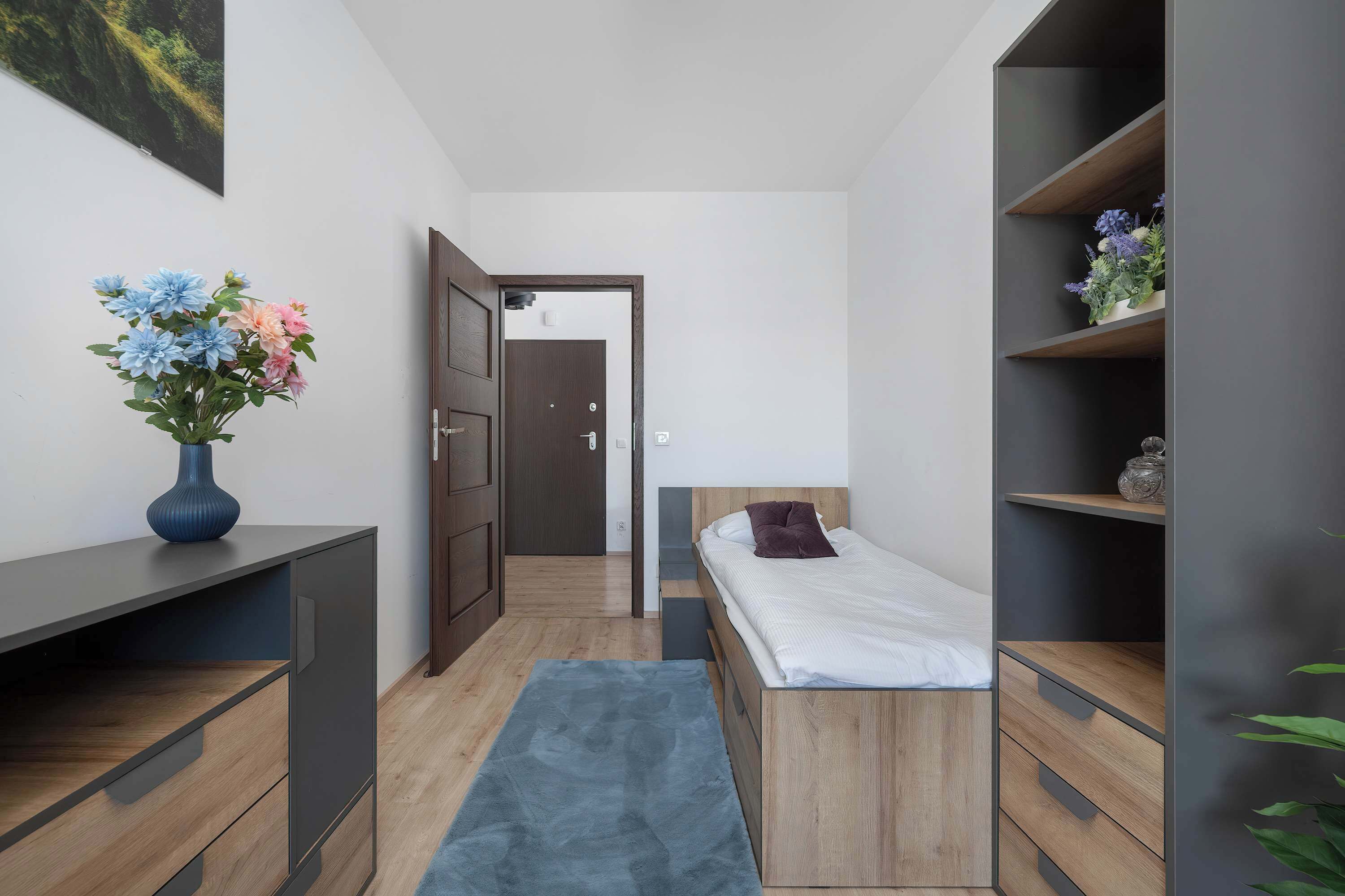 Une chambre moderne comprenant un lit, des tables de chevet, un bureau, une chaise, un tapis et une porte donnant sur une autre pièce.