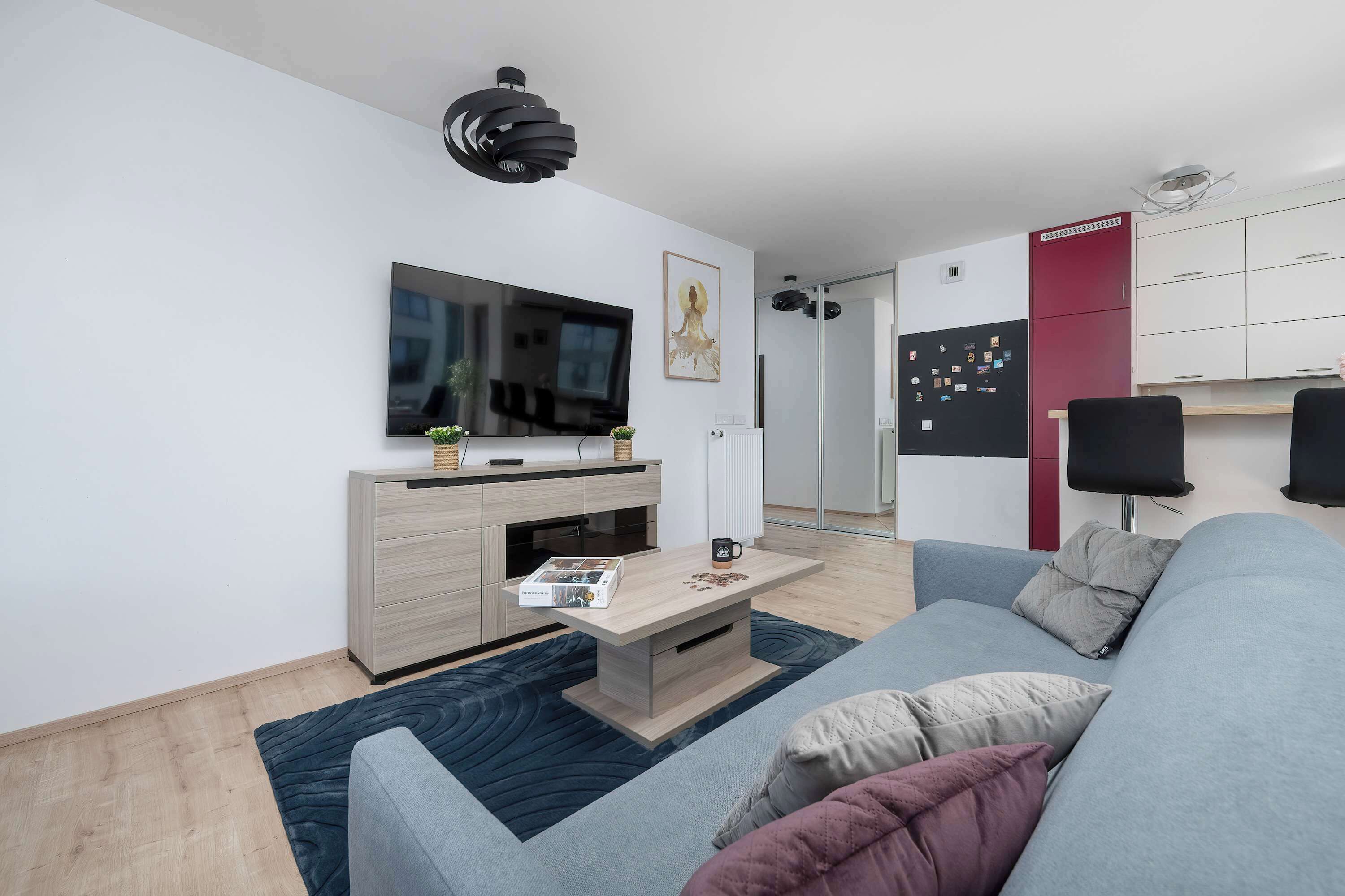 Een moderne woonkamer met een flatscreen televisie, een salontafel, een bank en een eethoek met een rode kast.